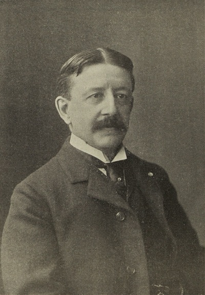 Portrait photograph of Durham White Stevens, a bearded man in a dark suit.